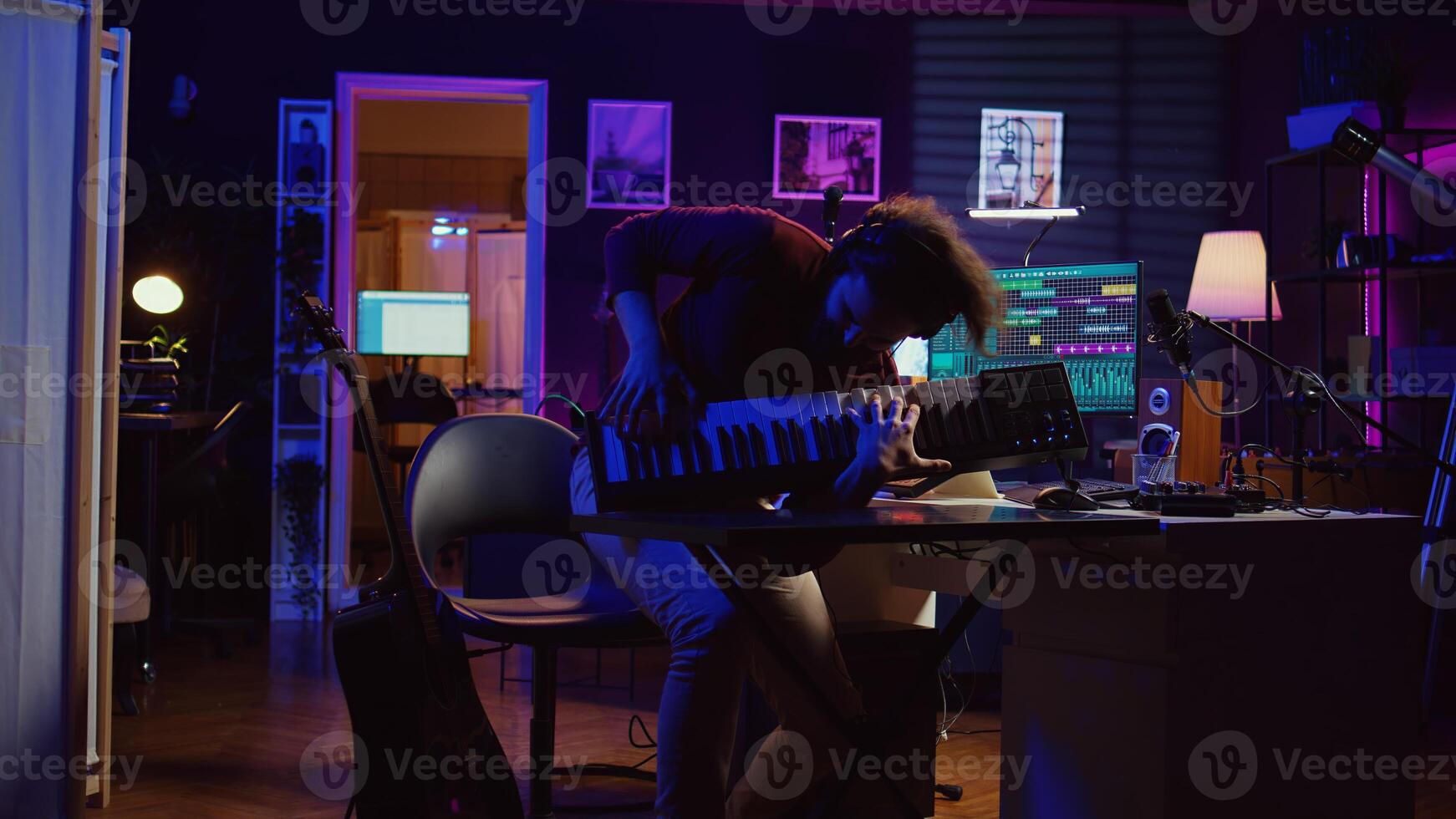 Energetic confident artist playing electronic piano in home studio, recording midi controller synthesizer notes to add audio effects. Cheerful sound engineer having fun with keyboard. Camera B. photo
