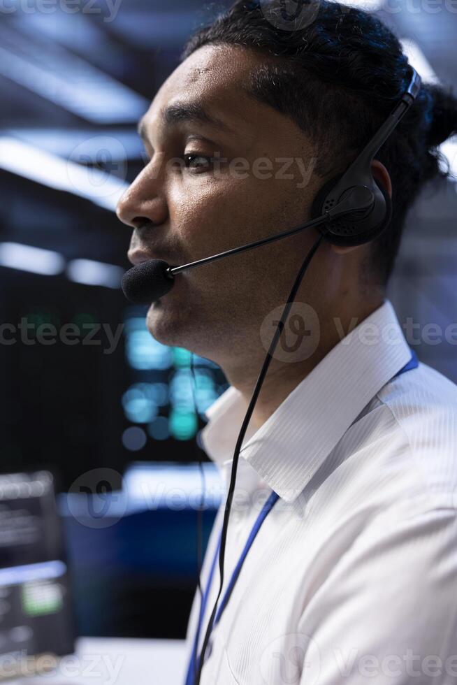 Data center agent supporting engineering team doing hardware maintenance, talking in headset microphone. Worker in high tech server room facility coordinating technicians using mic photo