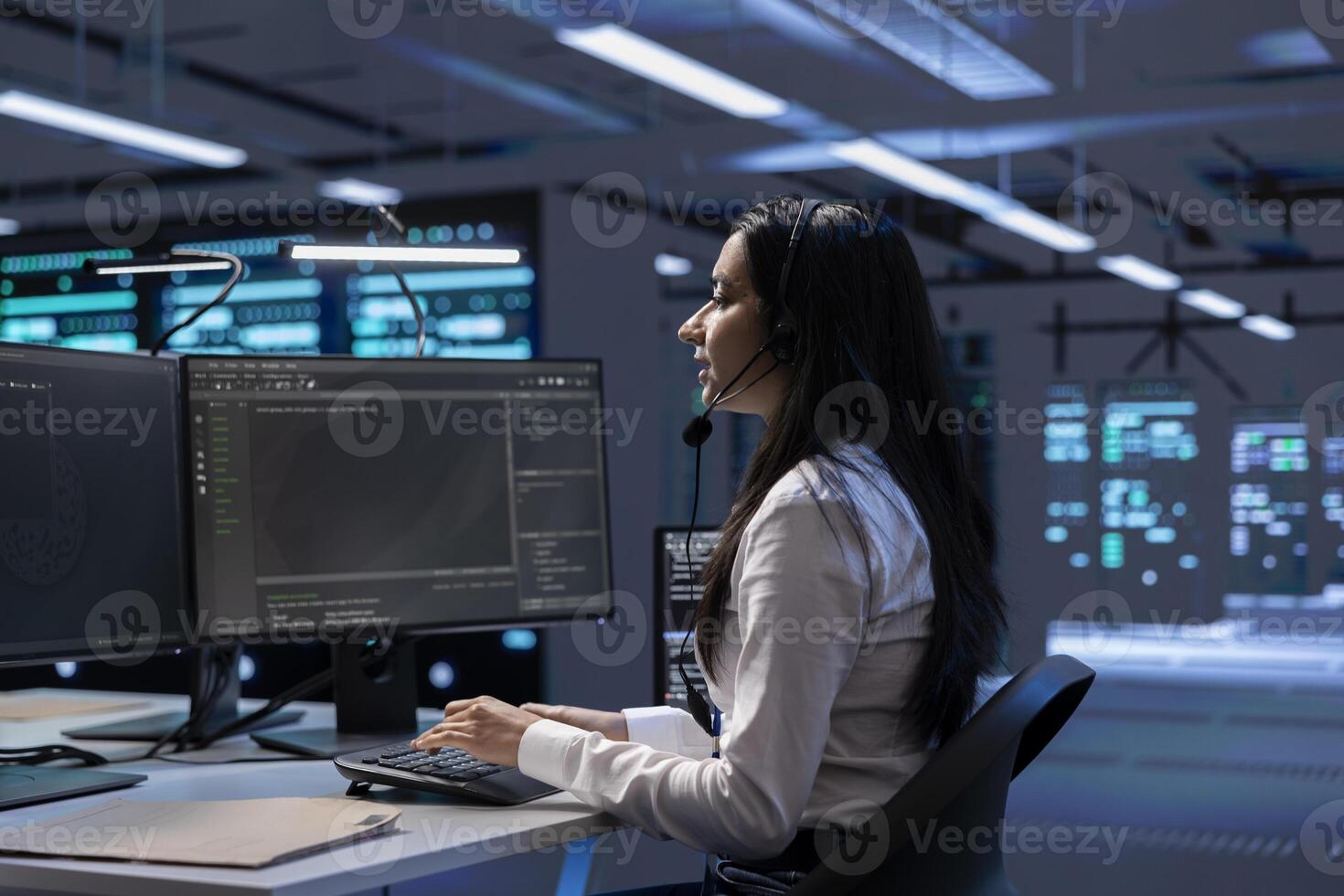 Data center support expert supporting engineering team doing equipment maintenance, talking in headset microphone. Woman in server farm coordinating technicians using mic photo