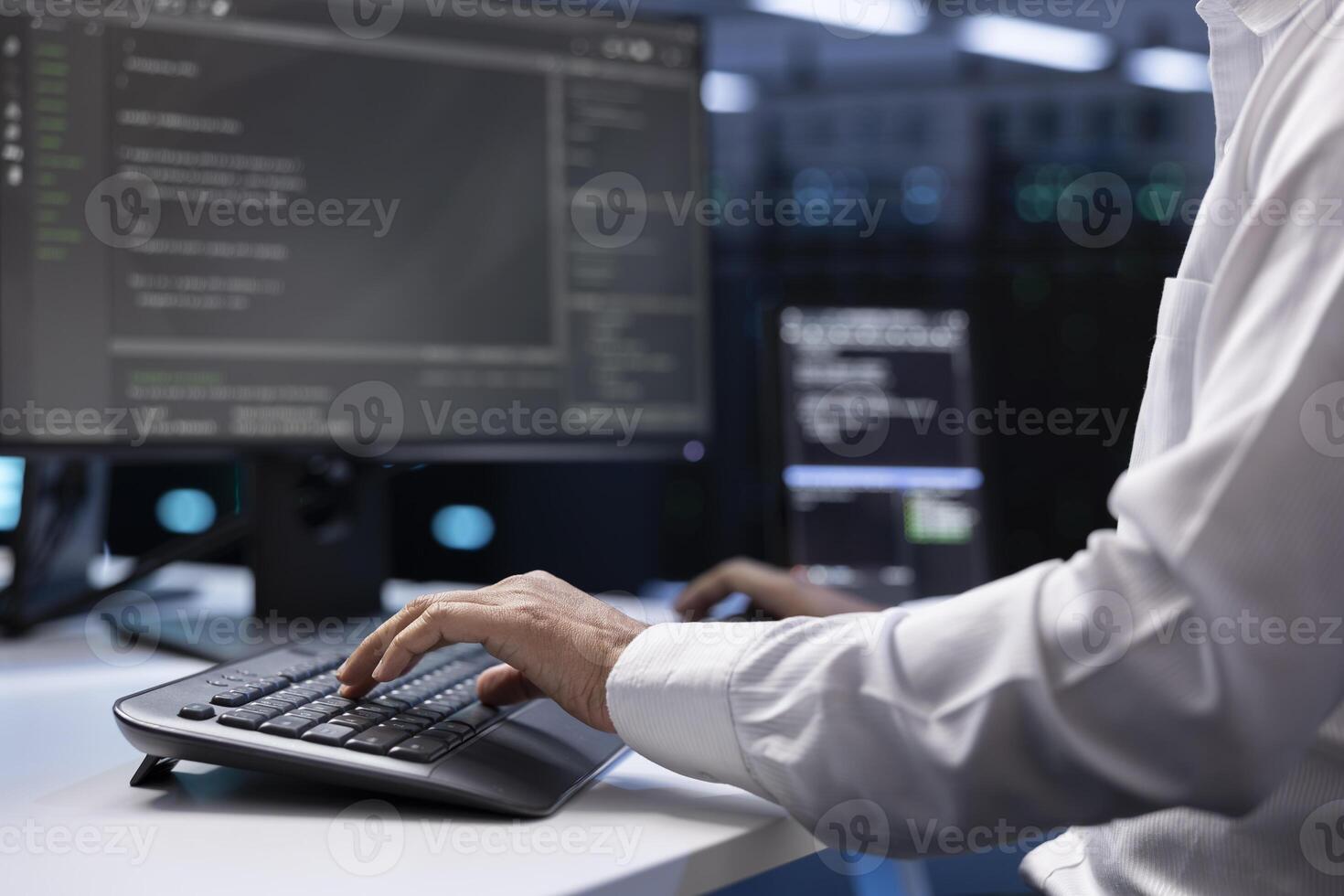 IT administrator working on PC in hardware room housing server rackmounts, storage devices and networking units providing vast amounts of computing resources, doing equipment maintenance, close up photo