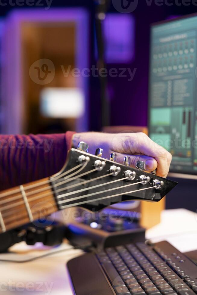 Skilled musician tuning his acoustic guitar strings to record new audio files in a home studio session, twisting the knobs in accord. Songwriter producing and editing new songs. Close up. photo