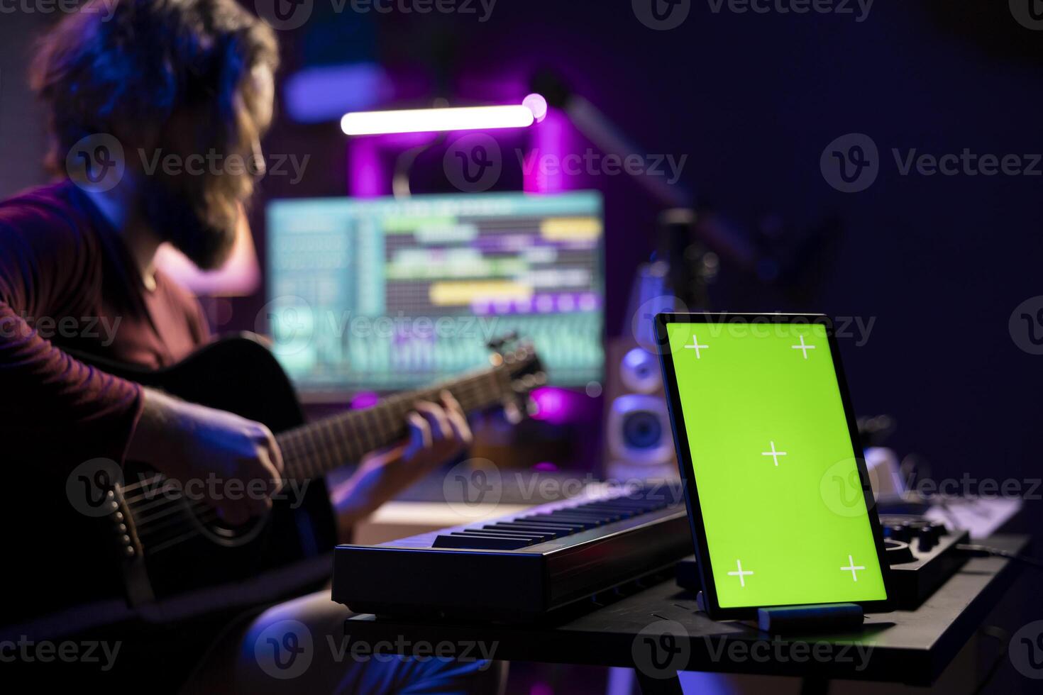 Audio engineer playing guitar and recording tunes on daw software, skilled artist learning to play new songs and strings accords. Music producer uses greenscreen on tablet, home studio. photo