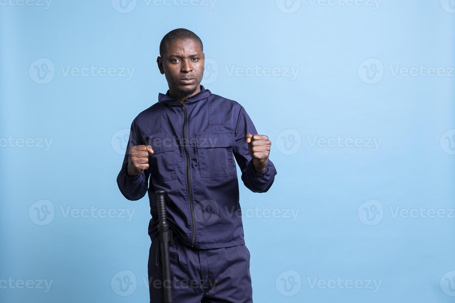 Professional security guard posing with clenched fists in studio, ready to throw punches while on duty. Male agent protecting the premises, taking safety measures and fighting if necessary. photo