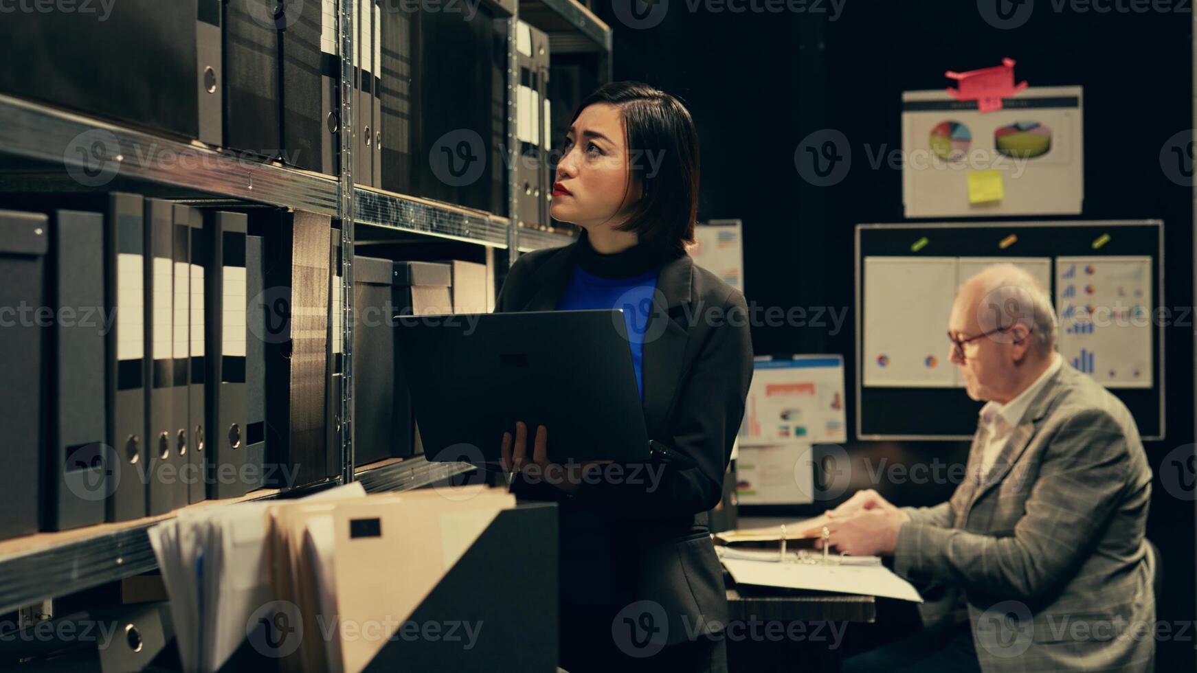 Detective evaluating old archived folders to organize all cases based on crimes, digitizes documents to preserve evidence on laptop. Private agent searching for forensics notes. Camera B. photo