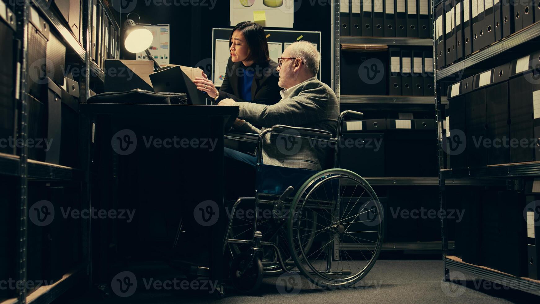 Inspector consulting with criminal expert on archived materials and autopsy records, examining folders and old cases to find connections. Private investigation in disability friendly space. Camera B. photo