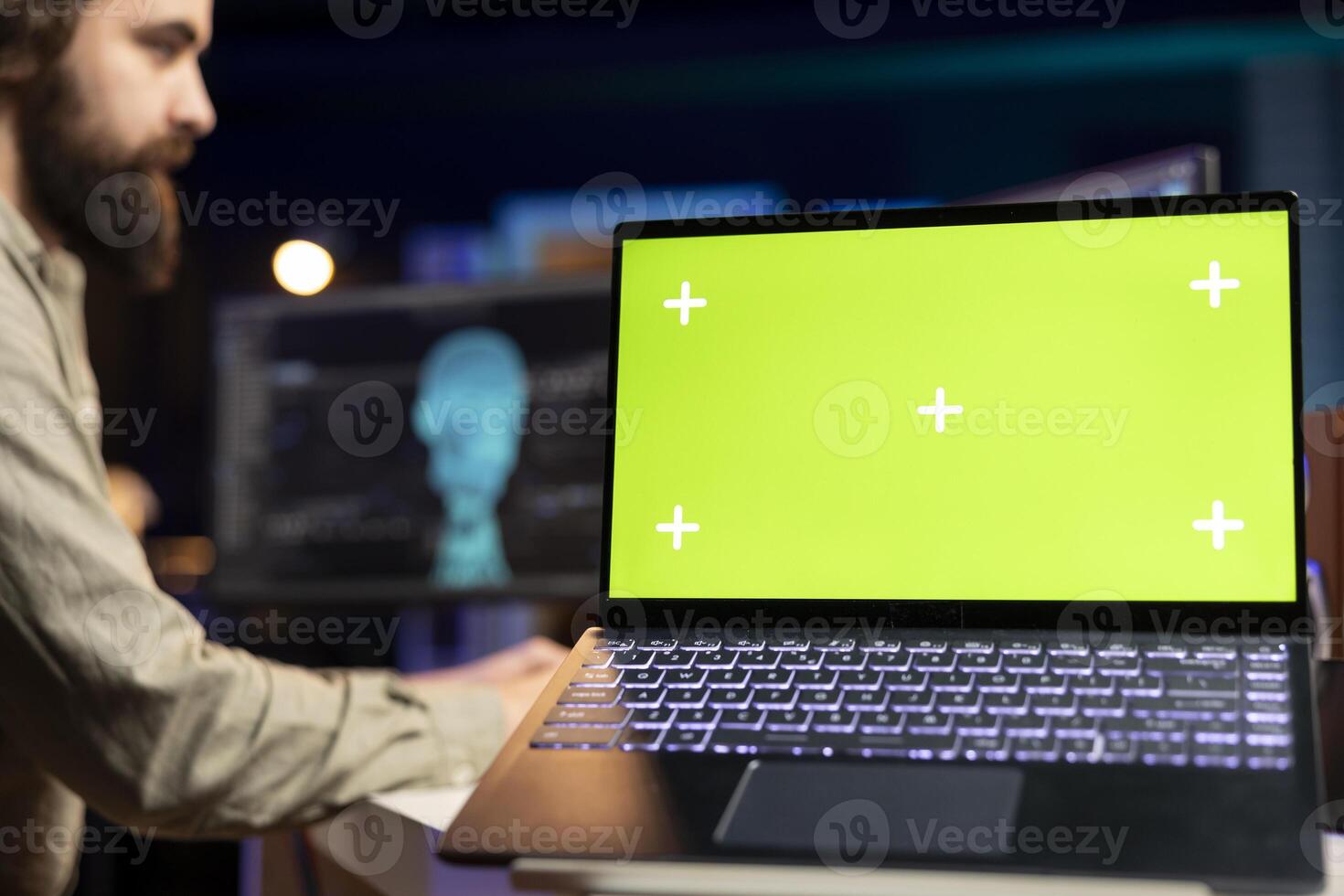 Focus on green screen laptop used by engineer wearing EEG headset in blurry background to upload consciousness into computer. Close up of mockup laptop used by IT expert to create upload brain photo