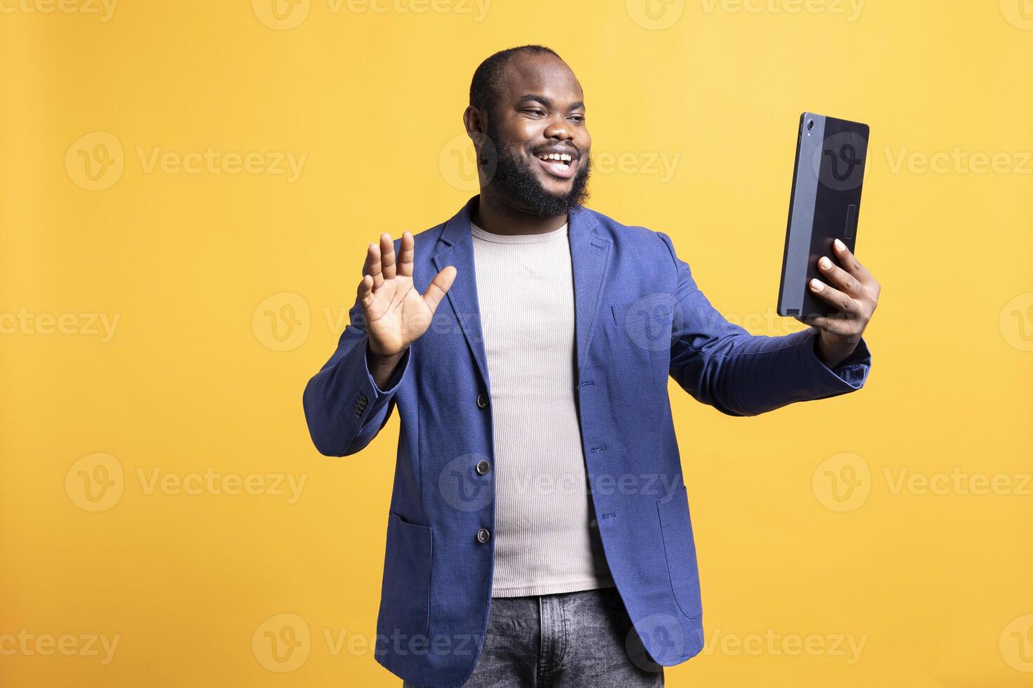 Jolly man excited to greet friends during teleconference meeting using tablet, studio background. Merry person waving hand, saluting mate during internet call on portable device photo