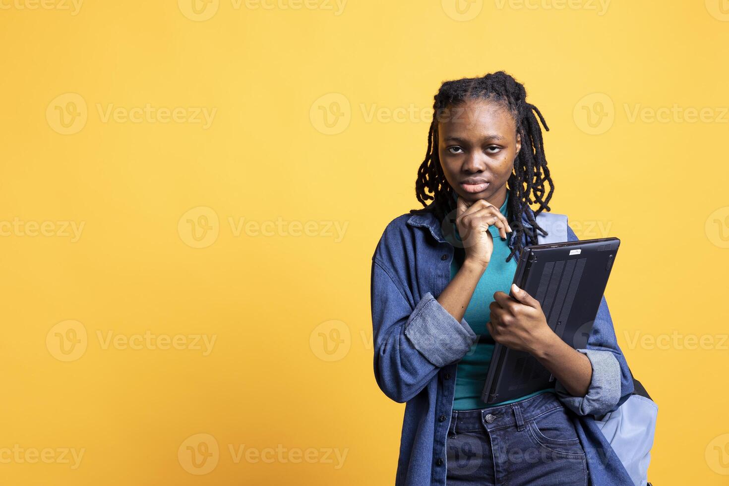 Portrait of pensive woman holding laptop, brainstorming during work shift, isolated over studio background. Employee with notebook doing thinking hand gesturing, ready to do tasks photo