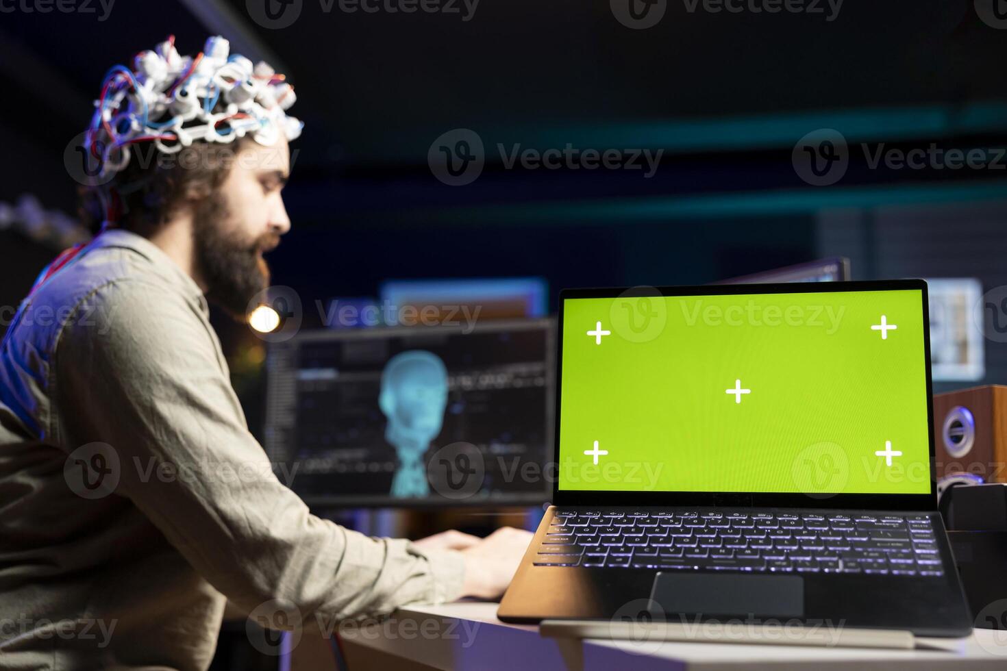 Focus on green screen laptop used by programmer using EEG headset to upload mind into PC. Close up of mockup notebook on desk next to man experimenting with transferring consciousness into cyberspace photo