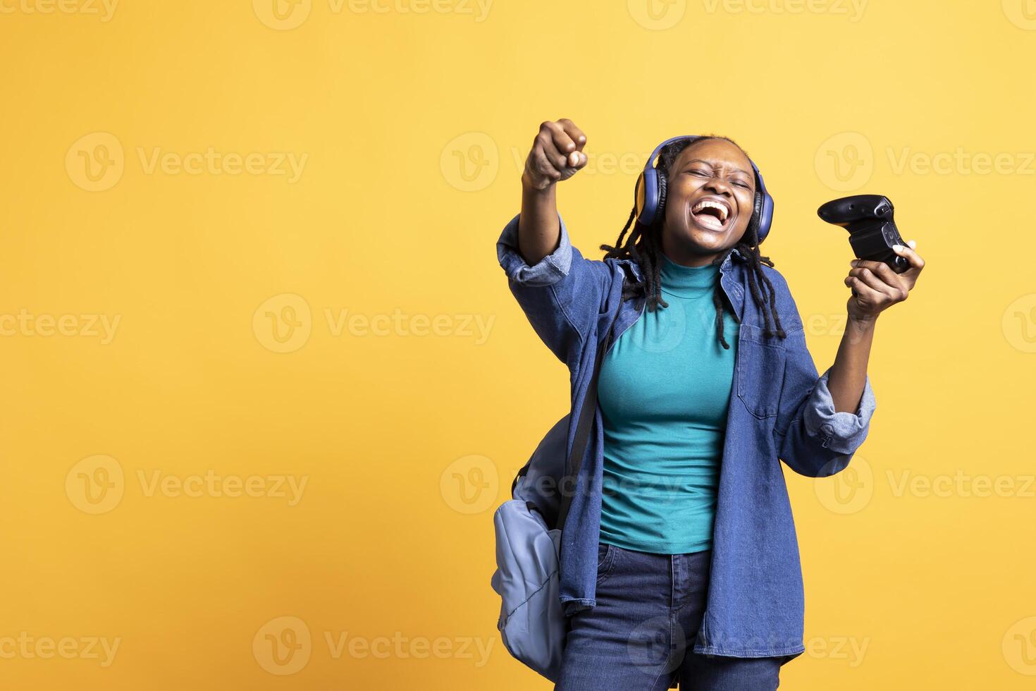 Euphoric african american teenager playing intense gaming console game, celebrating win, studio background. Ecstatic BIPOC young girl using controller, excited after being victorious in videogame photo
