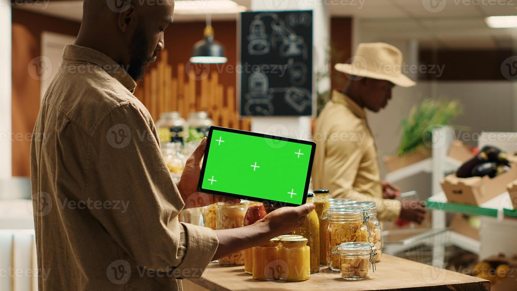 African american buyer shows tablet with greenscreen template in local grocery store, looking at blank copyspace next to chemicals free items. Regular client holds device with chromakey. Camera 1. photo