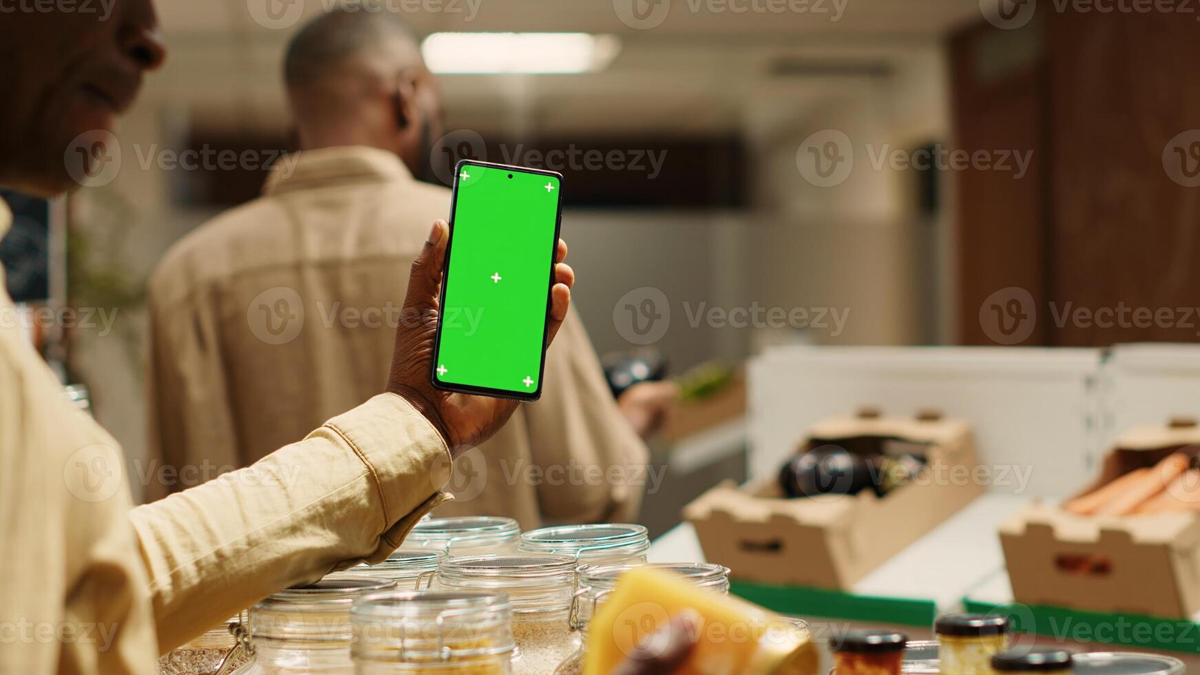 African american storekeeper holding phone with greenscreen in local grocery store, having organic products on sale. Vendor presents isolated chromakey display on smartphone, mockup layout. Camera 1. photo