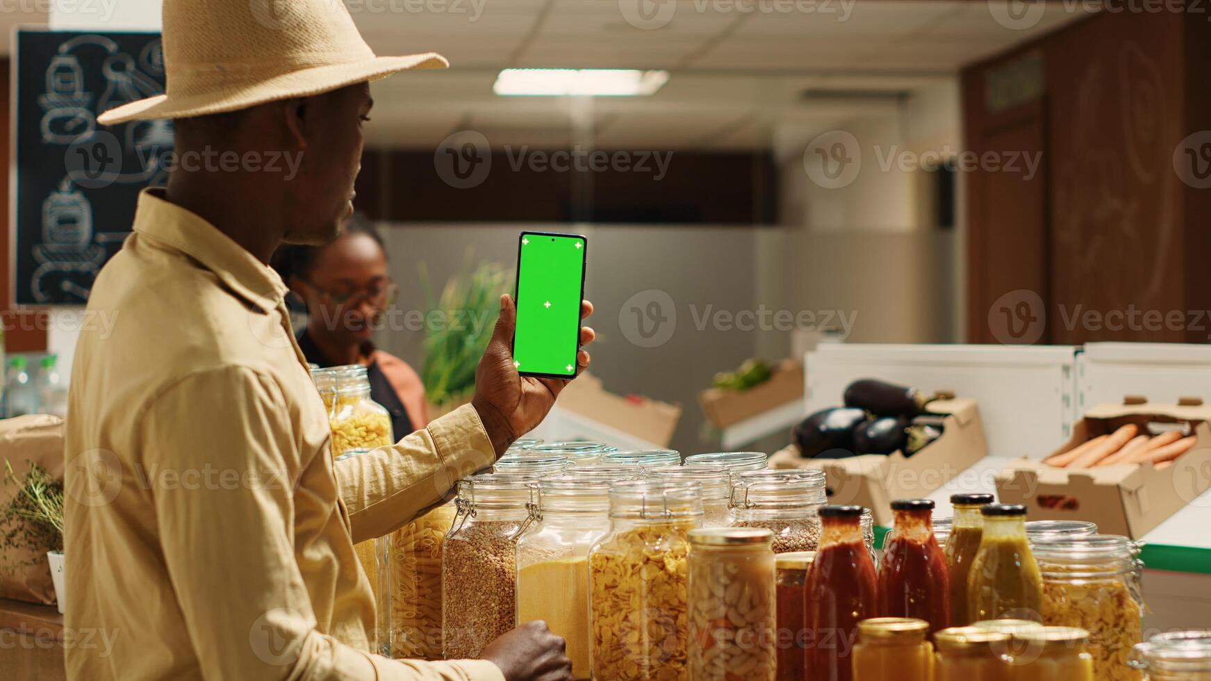 Business owner presenting blank greenscreen display on phone, showing isolated mockup layout in zero waste eco store. African american vendor using chromakey template on mobile phone. Camera 1. photo