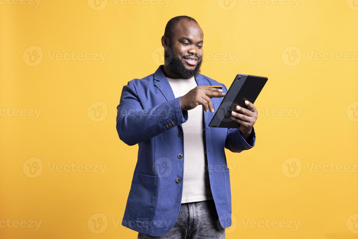 Smiling man adding payment method on website, enjoying sales period, isolated over studio background. Upbeat man doing internet shopping, typing credit card information on tablet photo