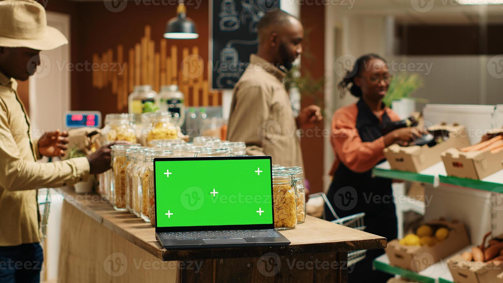 Laptop running isolated greenscreen on display in grocery store, presenting blank chromakey template on wireless pc. Clients and vendor checking organic ethically sourced products. Camera 1. photo