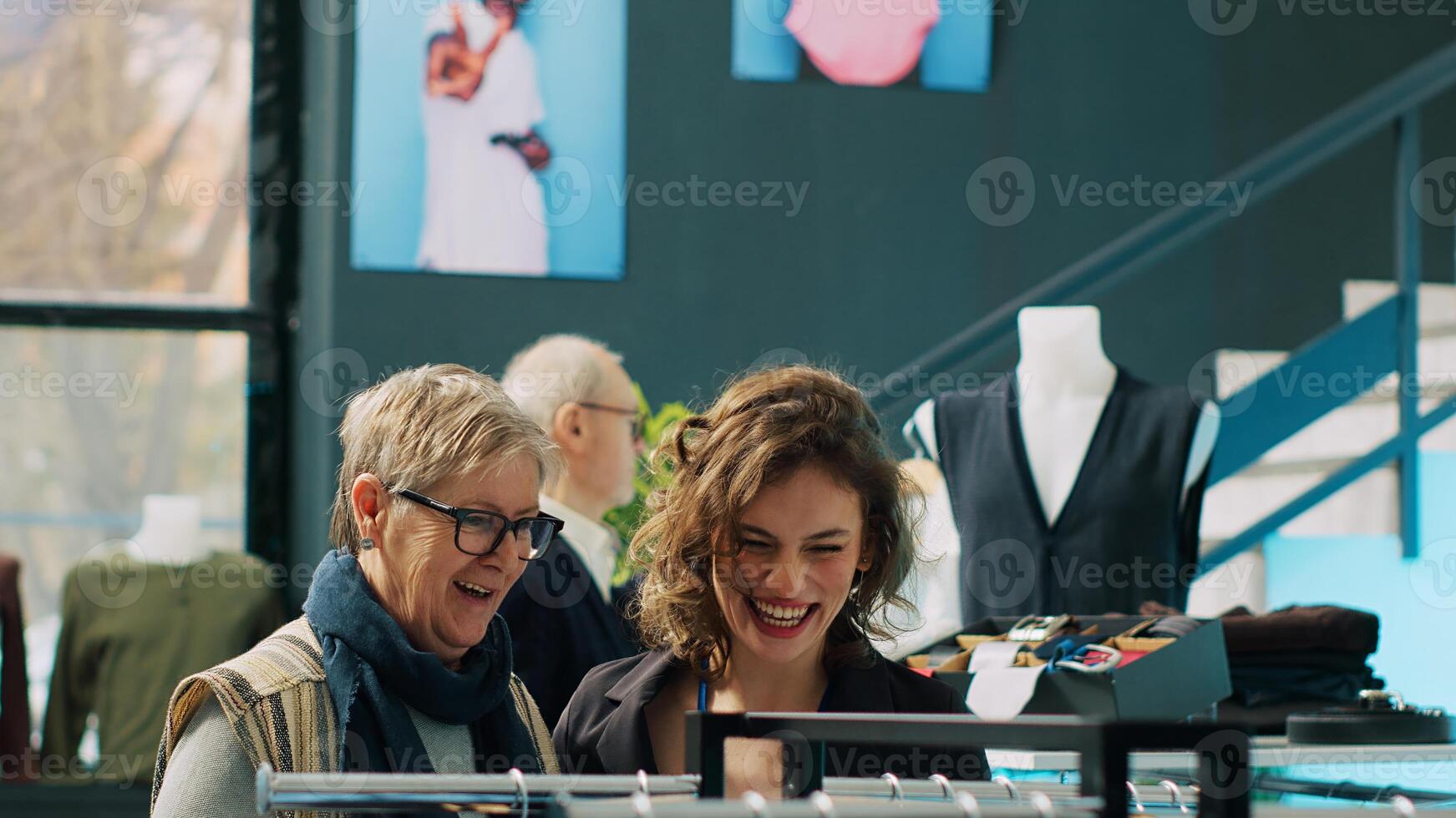 Clothing store employee makes fashion recommendations for client, helping senior woman to choose elegant shirt and suit jacket. Team of assistants suggesting trendy clothing items. Camera A. photo