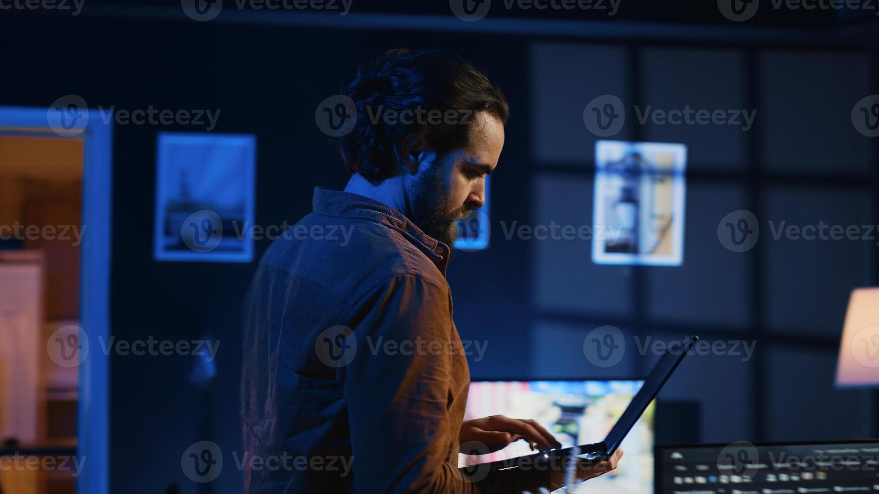 Man doing IT support job from home, walking around personal office with laptop in hand, coding. Nervous programmer wandering around room from stress, writing lines of code on notebook, camera A photo
