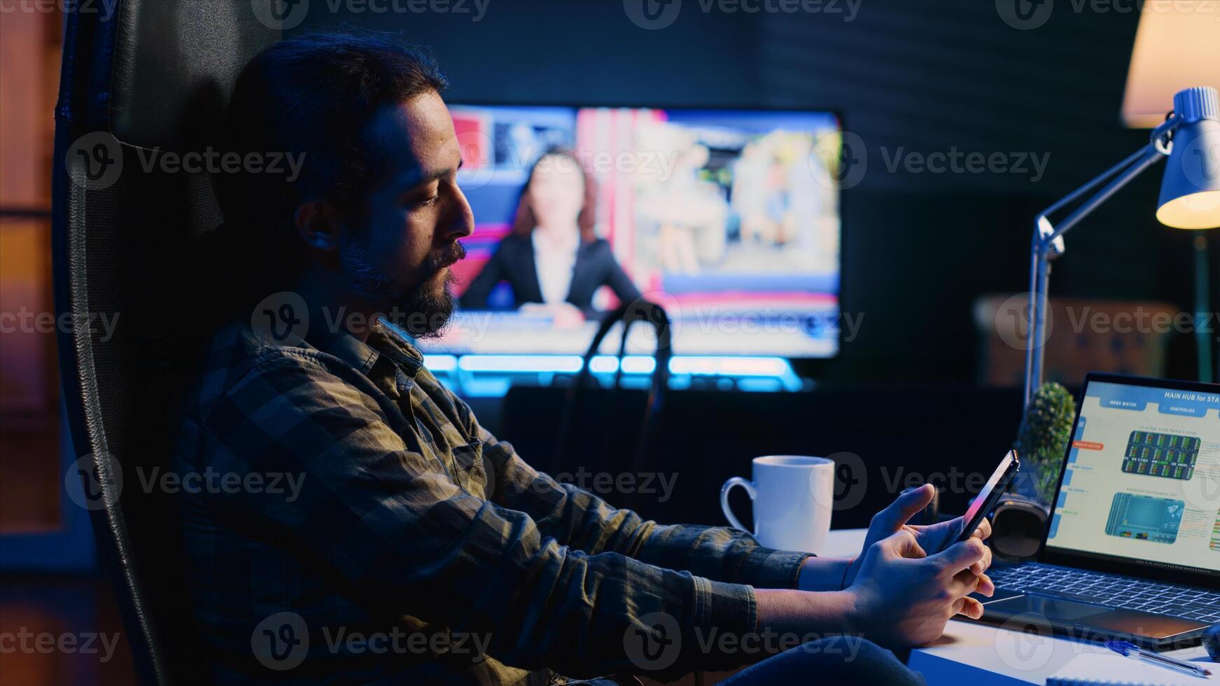 Man taking break from checking financial graphs on laptop, playing games on phone. Remote worker relaxing after analyzing business graphic figures, enjoying videogame on smartphone, camera A photo