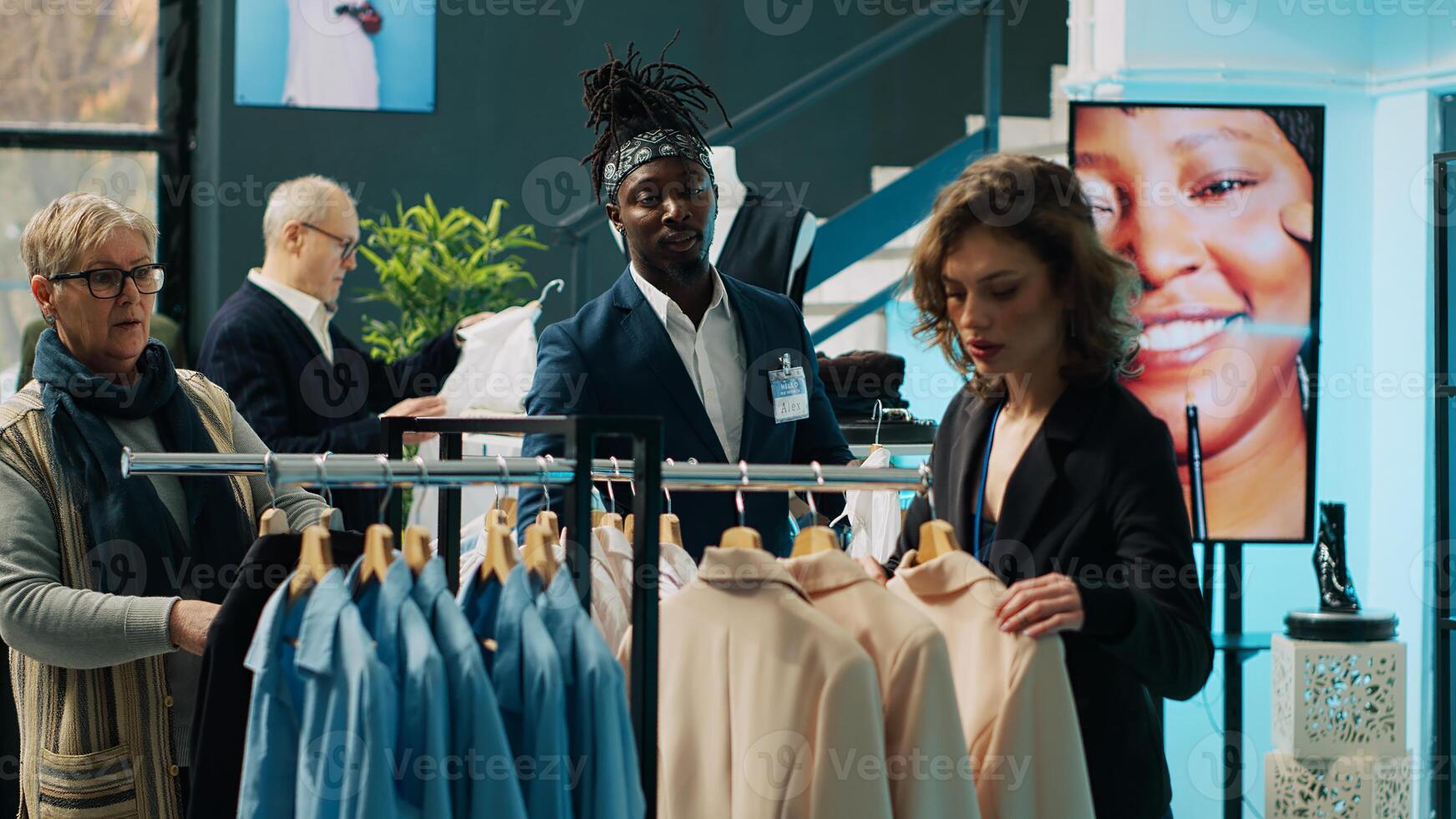 Employees team presenting variety of clothes to senior client, helping her to choose the perfect shirt size to create a formal outfit. Diverse store assistants show clothing from designers. Camera A. photo