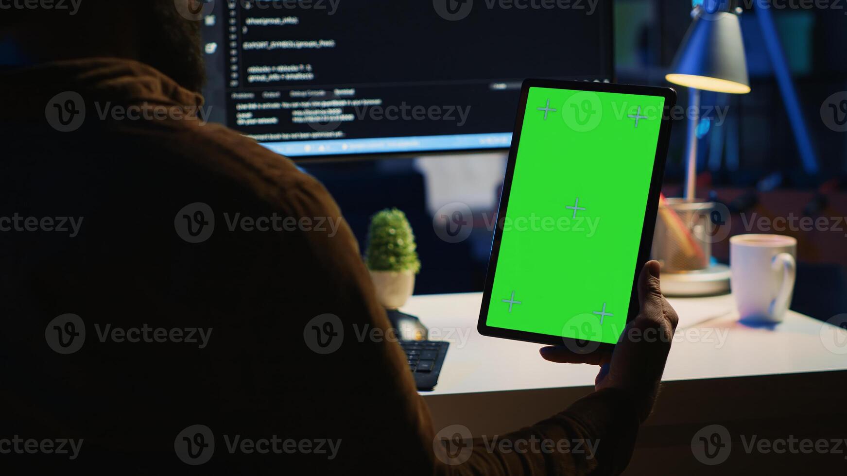 Software developer programming in home office, crosschecking lines of code between green screen tablet and PC screen. IT admin holding mockup portable device while coding on computer photo