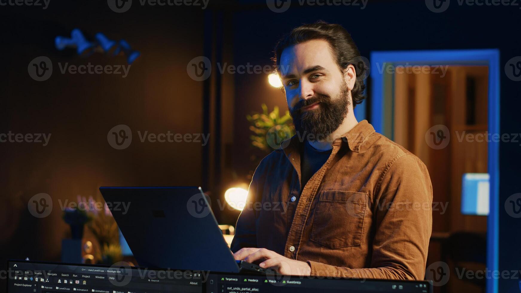 Portrait of smiling man doing IT support job from home, standing in personal office with laptop in hand, coding. Cheerful programmer writing lines of code on notebook in living room, camera A photo