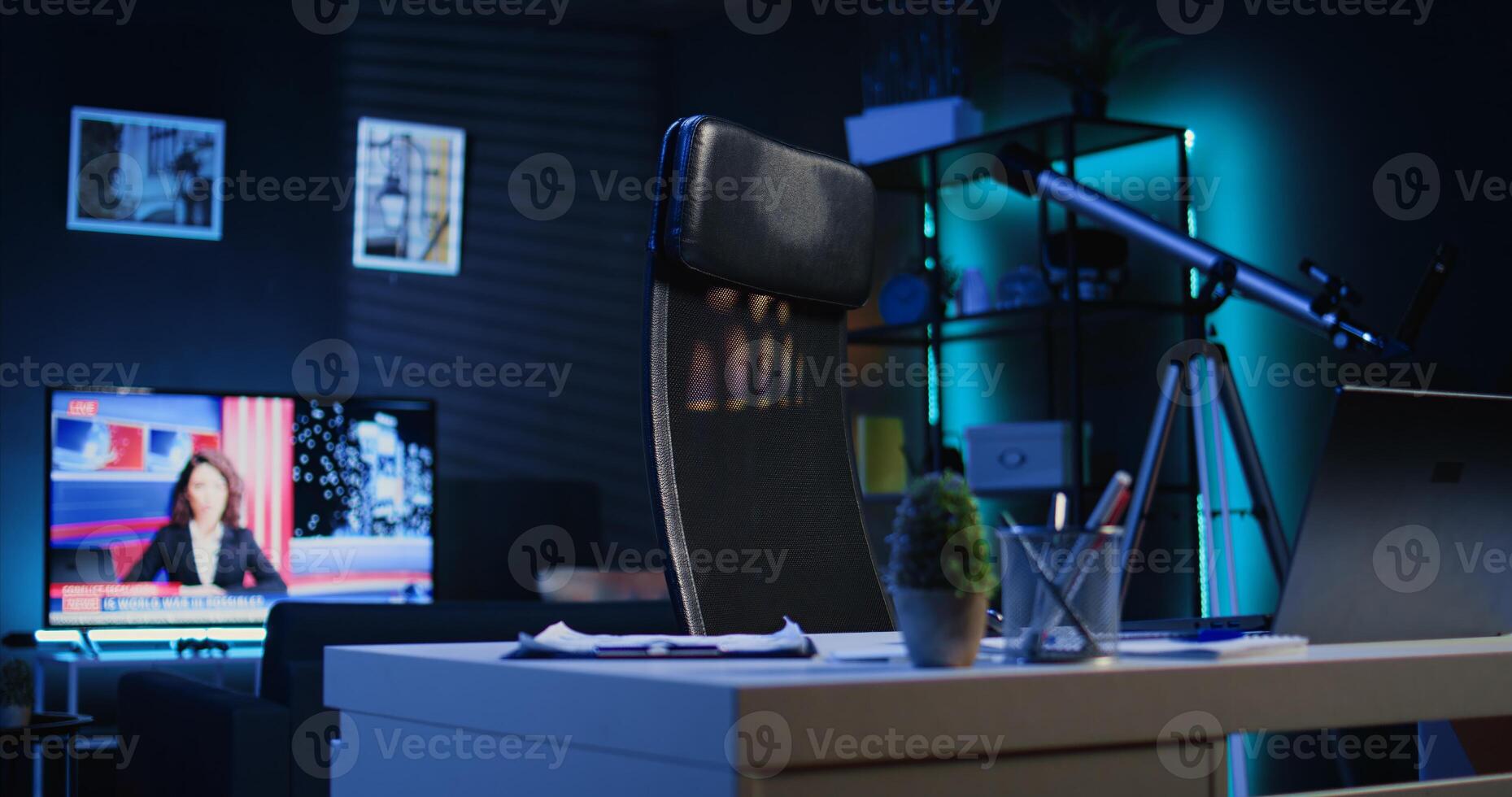 Dimly lit apartment with office desk in front of smart TV displaying news program broadcasting. Laptop on table and television screen in empty room showing channel, camera B close up shot photo