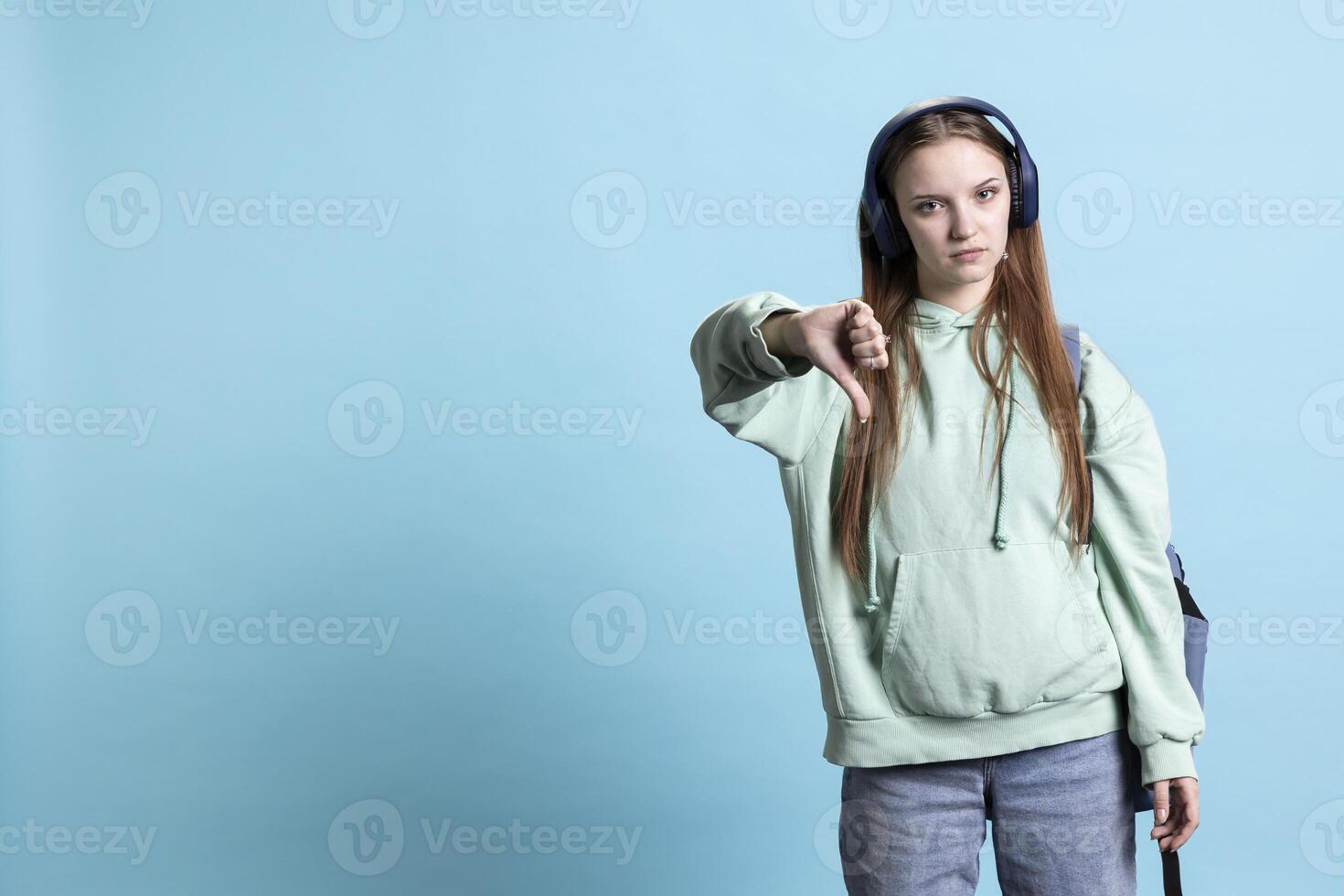 Frustrated woman showing thumbs down sign gesturing, disapproving and offering negative feedback. Disappointed girl doing dislike hand gesture, isolated over studio background photo