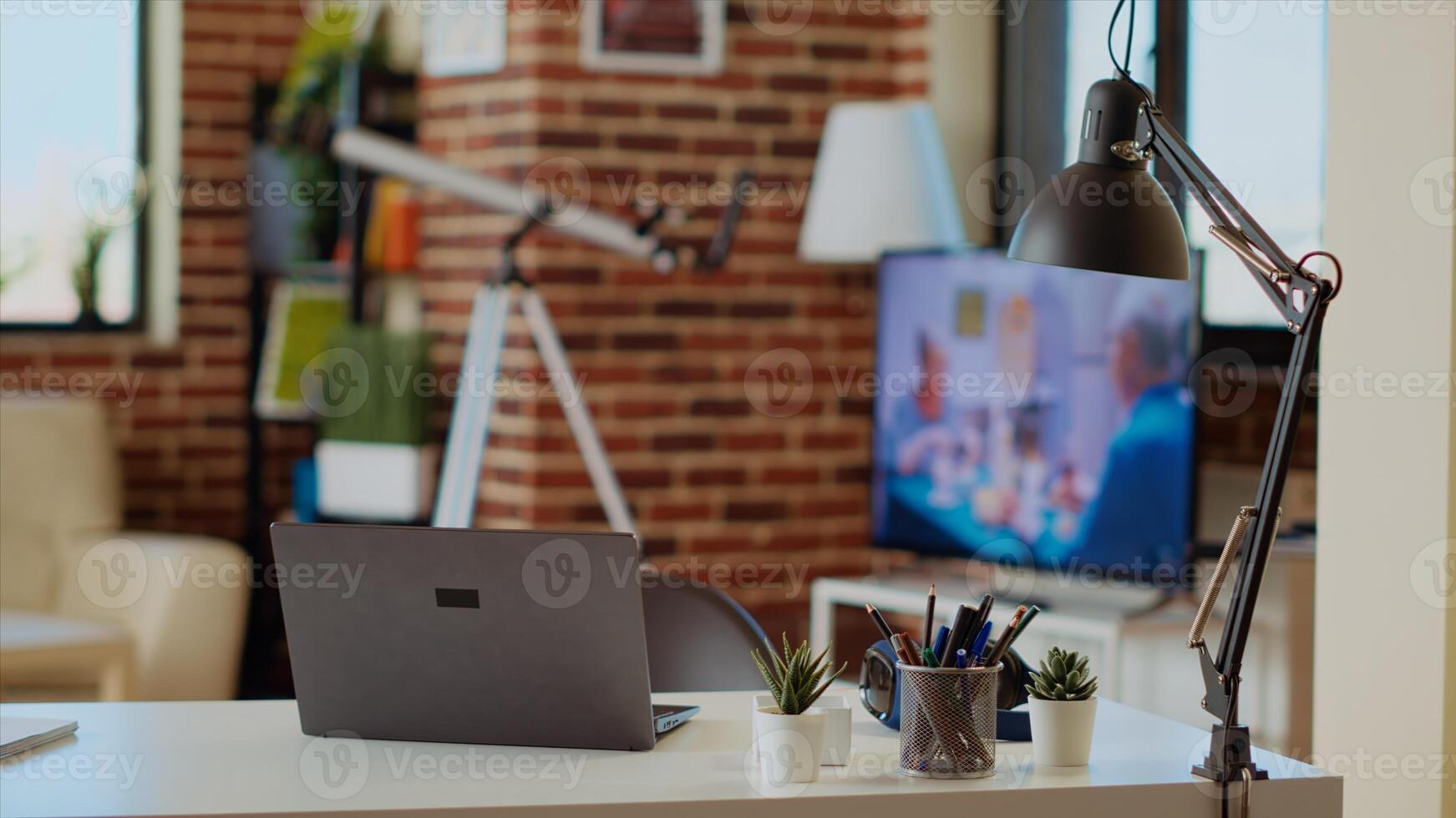 Cozy stylish empty apartment panning shot with TV left open in background and laptop on table desk. Bright modern living room with brick walls and nice interior design, close up photo