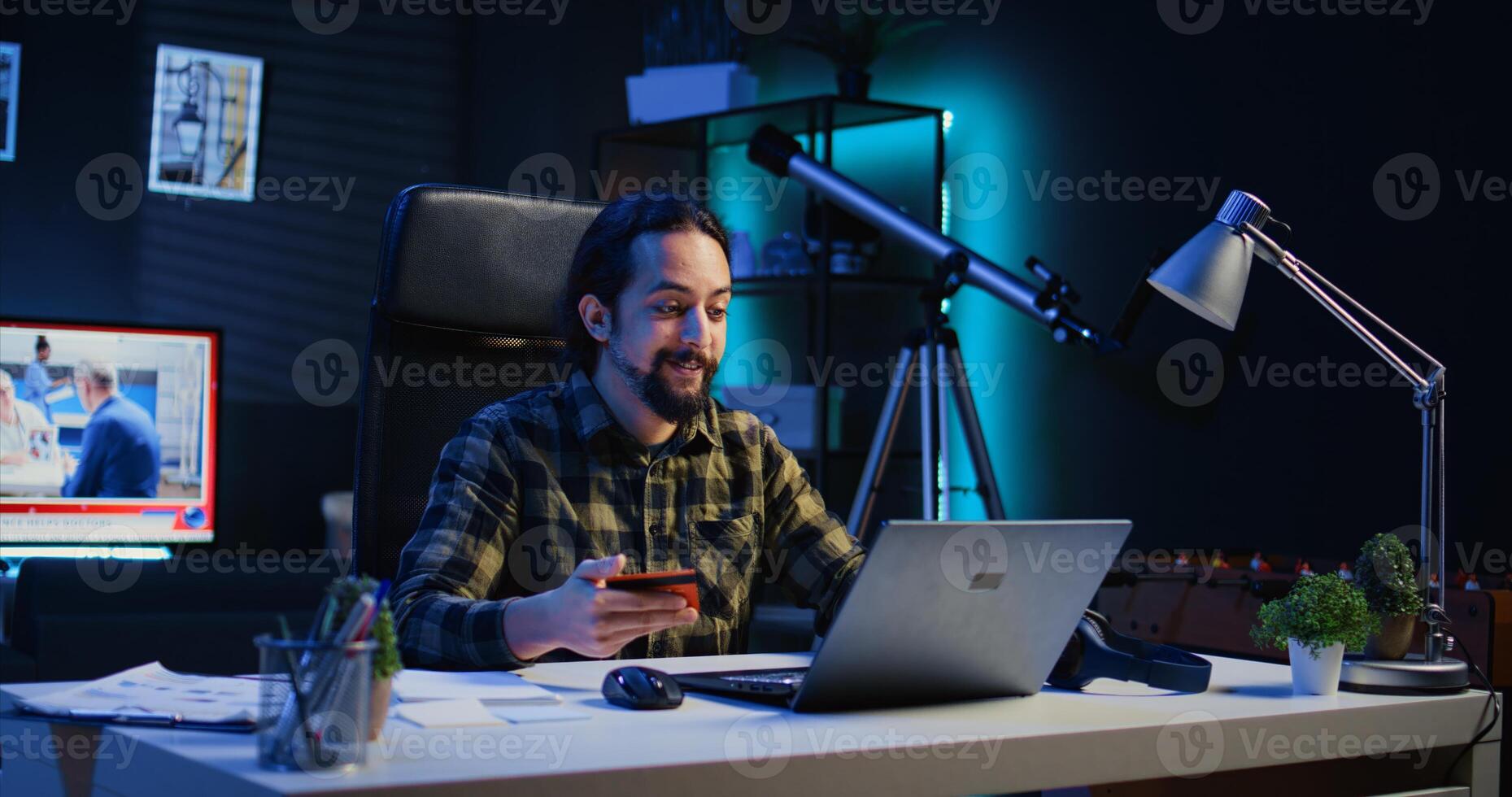Happy man doing internet shopping, carefully typing credit card information on laptop in apartment. Smiling person adding payment method on website while in living room, camera B photo