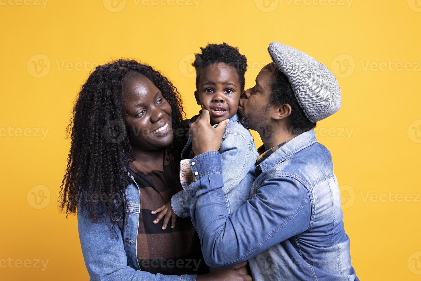 Affectionate father kissing his little son on the cheek, happy loving family of three posing in studio. African american couple holding their toddler and bonding together, showing love and respect. photo