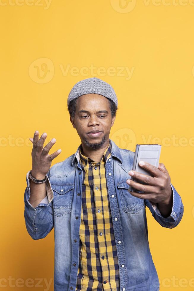 African american masculine person reads his text messages on his phone, checking social media account and webpages. Cool bearded man connects with people on internet network in studio. photo
