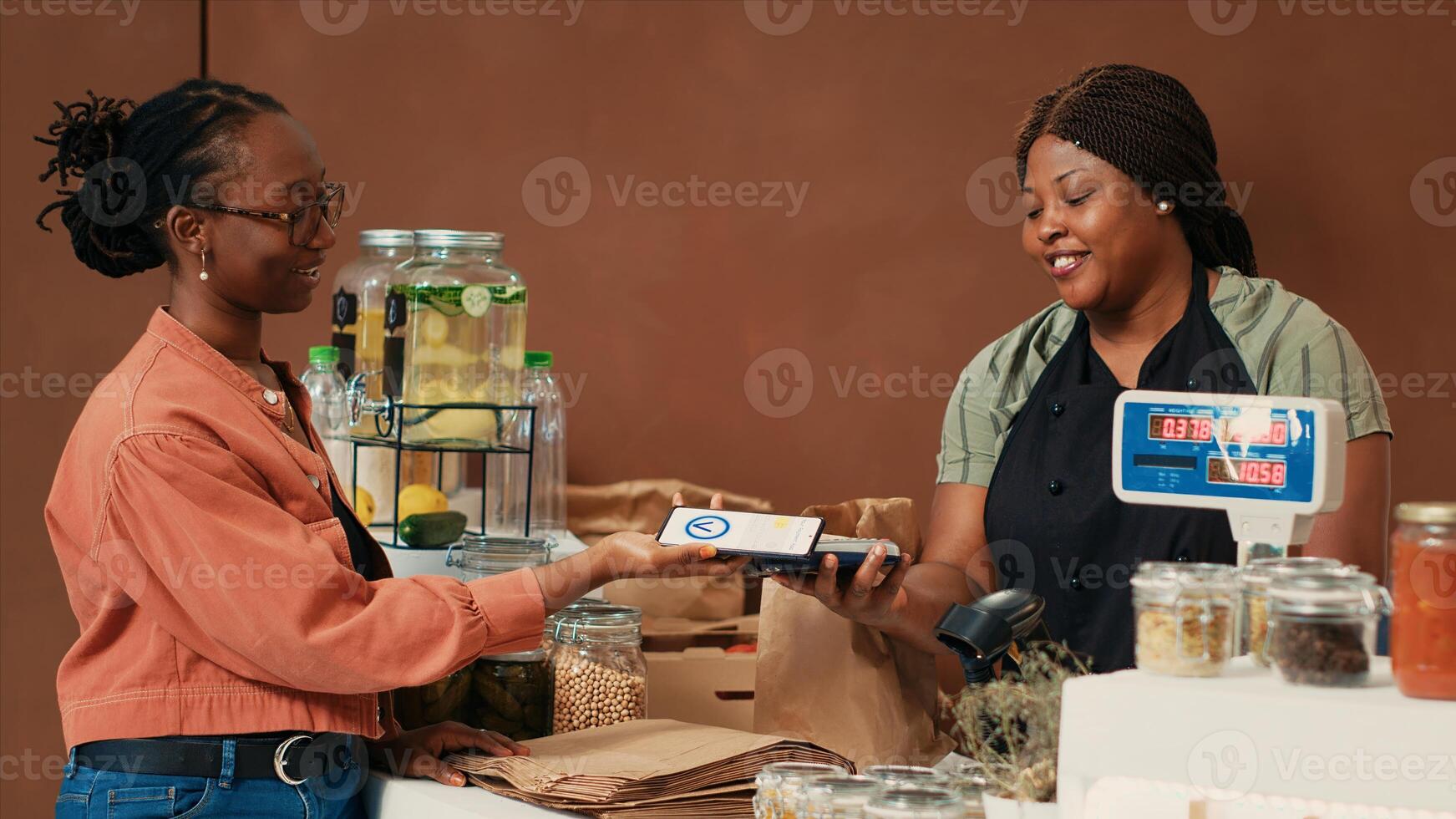Customer using mobile payment to buy organic farming produce from local grocery store, supporting sustainable lifestyle and healthy eating. African american vendor and client chatting at checkout. photo
