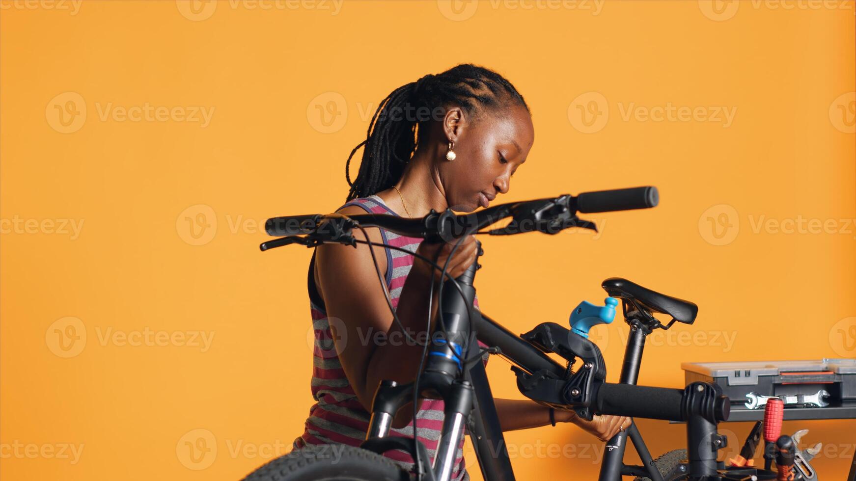 BIPOC mechanic setting up bike repair stand, using it to adjust handlebar and fix broken wheels, studio background. Professional placing bicycle on workstand in tight grip to inspect it, camera A photo