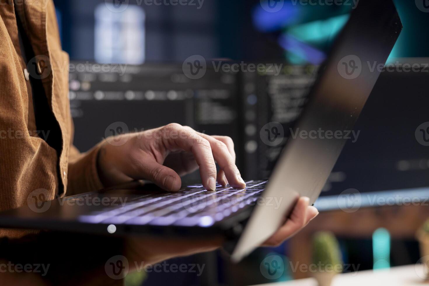 Computer scientist working from home using laptop, testing and deploying programs. Programmer checking code displayed on desktop PC screens in blurry background, close up shot photo