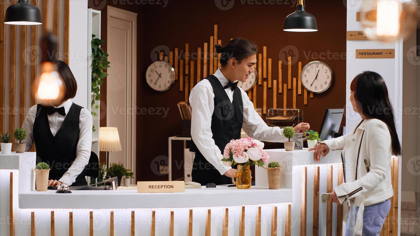 Asian guest arriving at hotel and asking about room reservation, talking to receptionist about check in process. Front desk staff team greeting customer at reception, presenting leisure facilities. photo