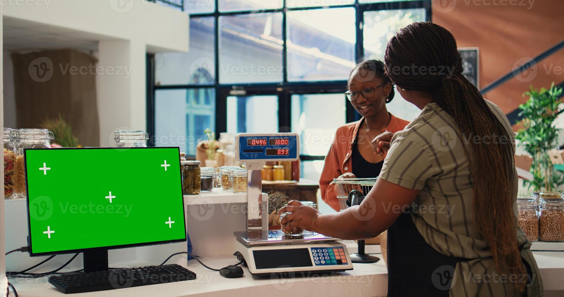 Buyer approaching checkout next to greenscreen display in local zero waste eco store, merchant working with isolated copyspace and mockup layout on computer. Blank chromakey layout. Tripod shot. photo
