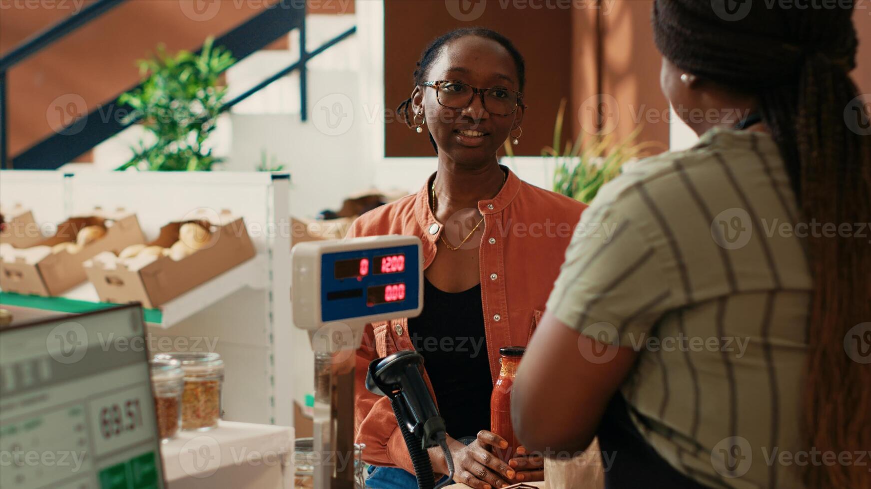 Organic store merchant scanning jars for customer at checkout, selling homemade additives free sauces and grains in recyclable jars. African american buyer looking for fresh natural pantry supplies. photo