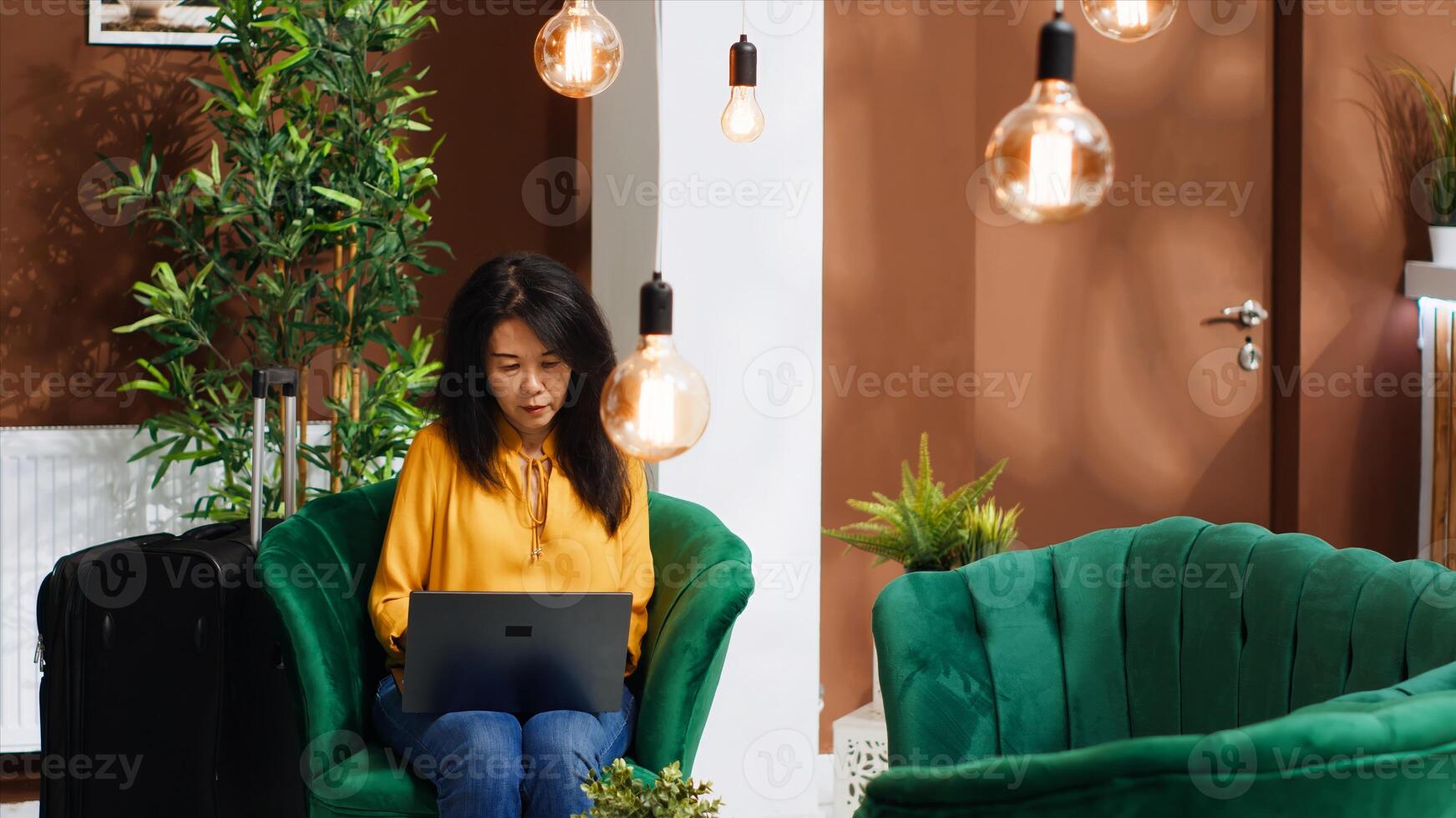 Asian tourist creating trip itinerary to visit landmarks, using internet while she waits for check in process. Hotel guest arriving early at reception, searching for famous places on laptop. photo
