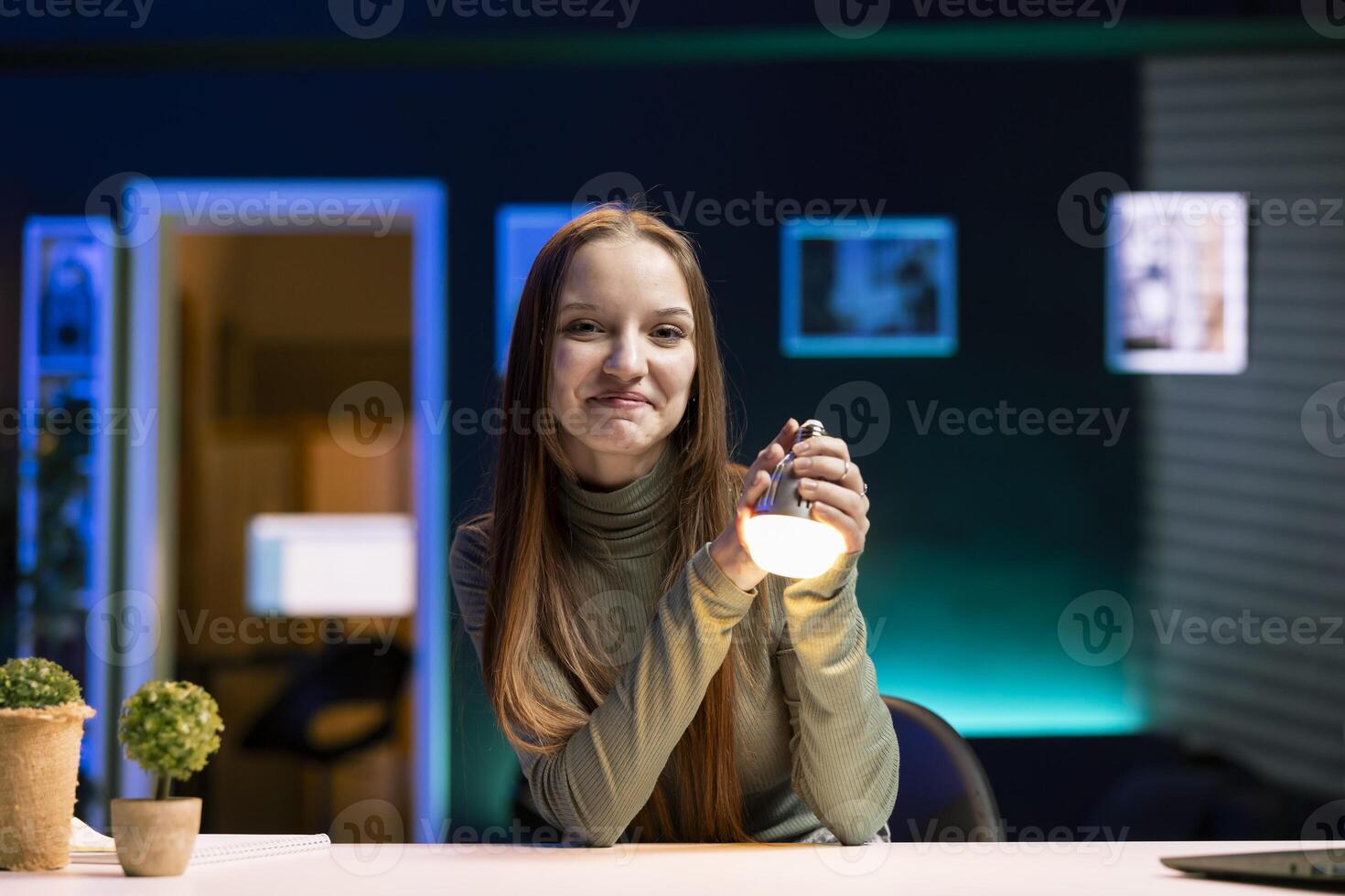 Portrait of smiling girl doing house improvement vlog, showcasing newly launched smart light bulb to viewers. Cheerful gen Z entertainer greeting fanbase, presenting WIFI home automation photo