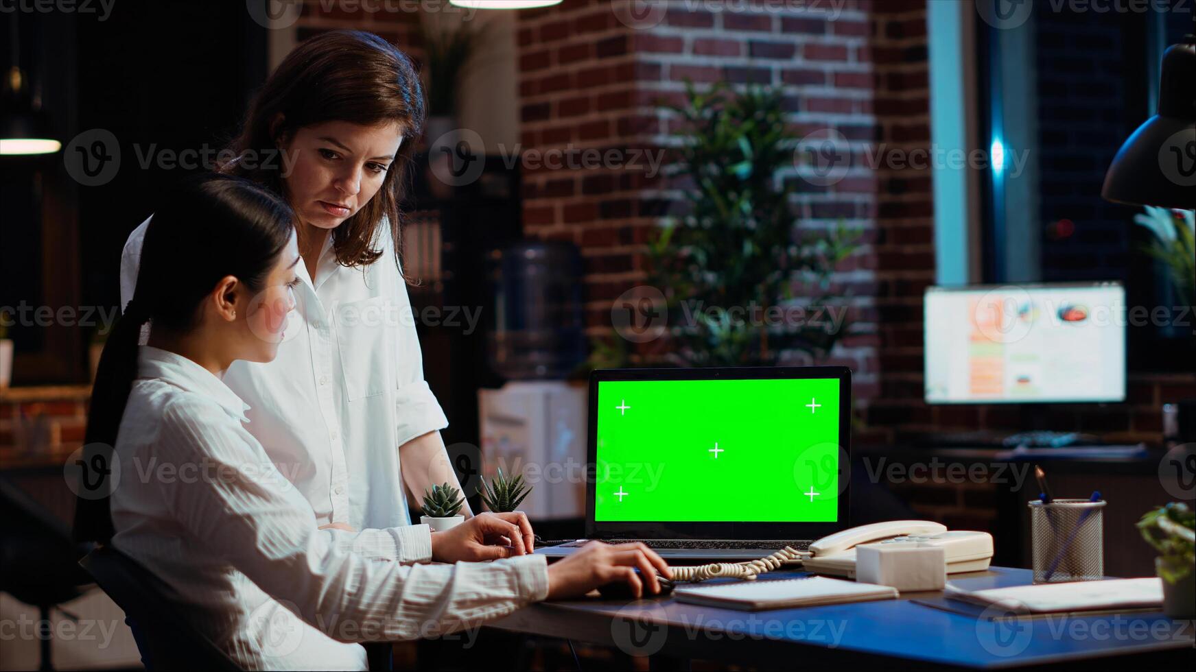 Businesswomen researching for company project, looking at documents on green screen laptop. Coworkers looking over accounting figures on chroma key electronic device display in office photo