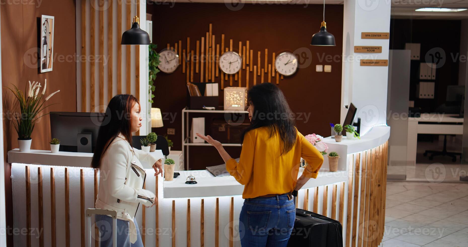 Asian women arriving at empty hotel reception and ringing bell for service, calling employees to provide assistance for registration. Clients with luggage requesting support from concierge staff. photo