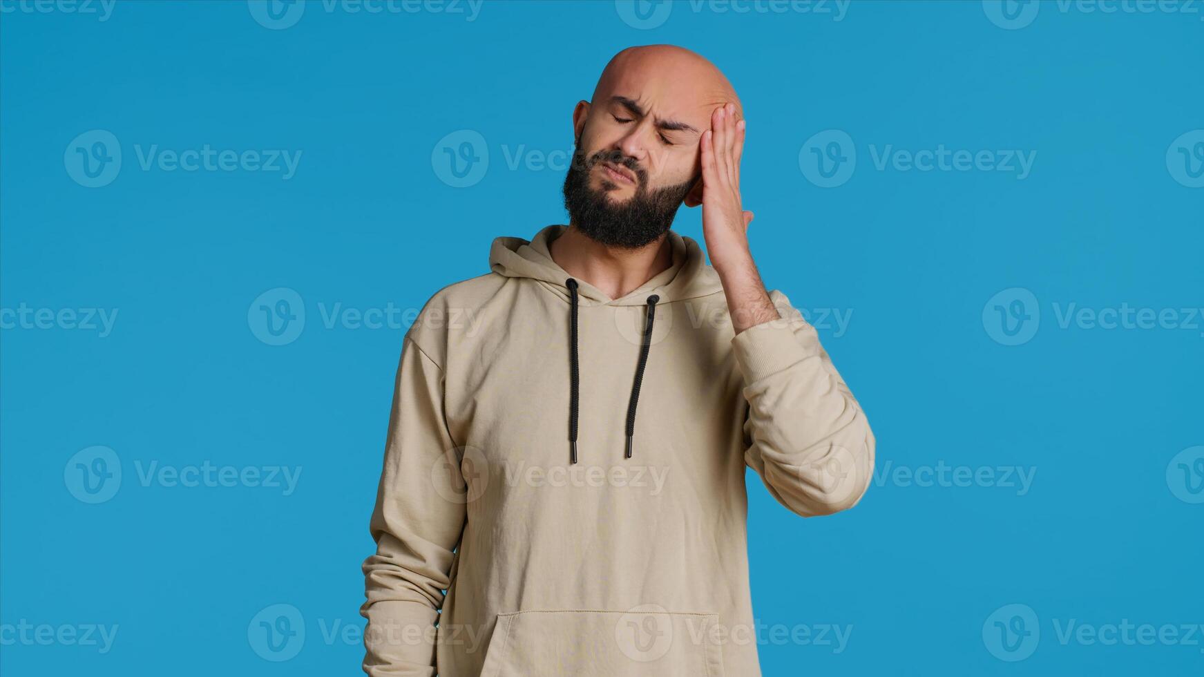 Unwell arab model dealing with serious headache in studio, feeling sick with a painful migraine and rubbing temples to ease the pressure. Tired person suffering from pain and tension. Camera 1. photo