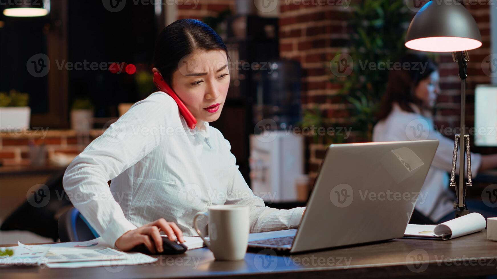 Company secretary taking phone call at office desk, answering customer inquiries while working on laptop, multitasking. Stressed worker having conversation on telephone and crosschecking data photo