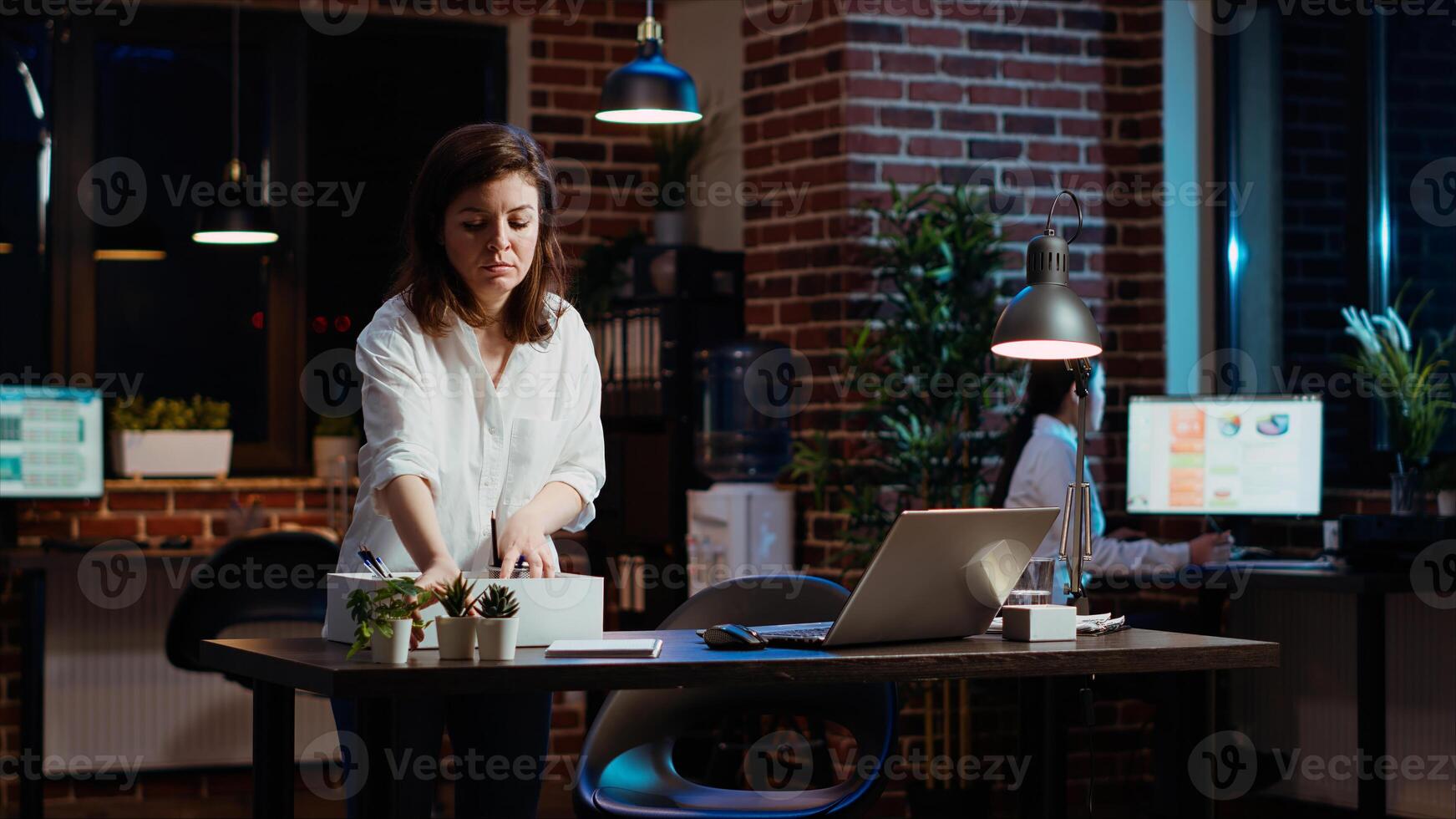 Frustrated employee packing desk belongings after being fired, saying goodbye to coworker. Upset employee preparing to leave office after being discharged by company management, camera B photo