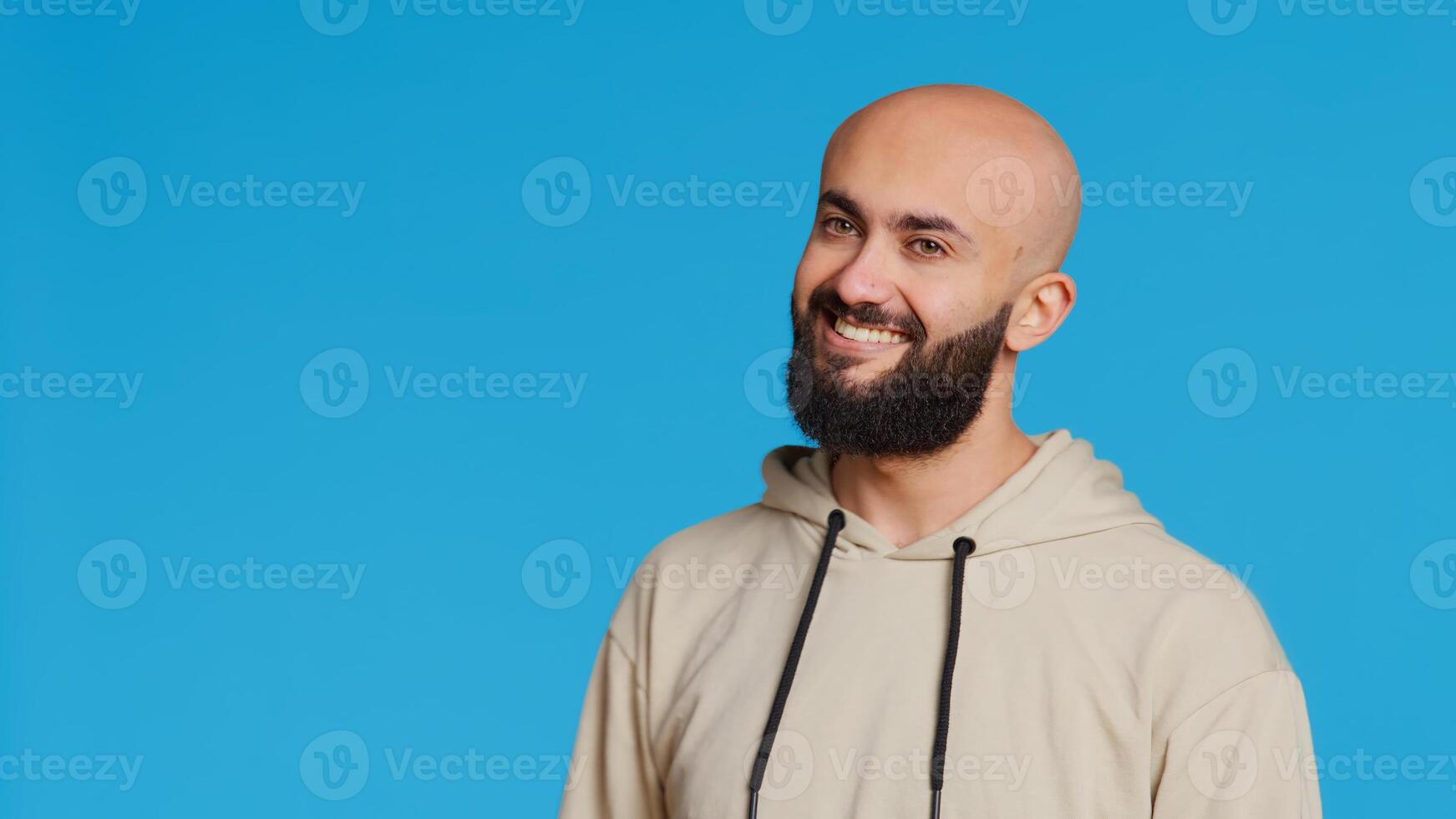 Middle eastern guy greeting people in front of camera, waving hello and smiling over blue background. Young person posing with confidence in studio, feeling confident and joyful. Camera 2. photo