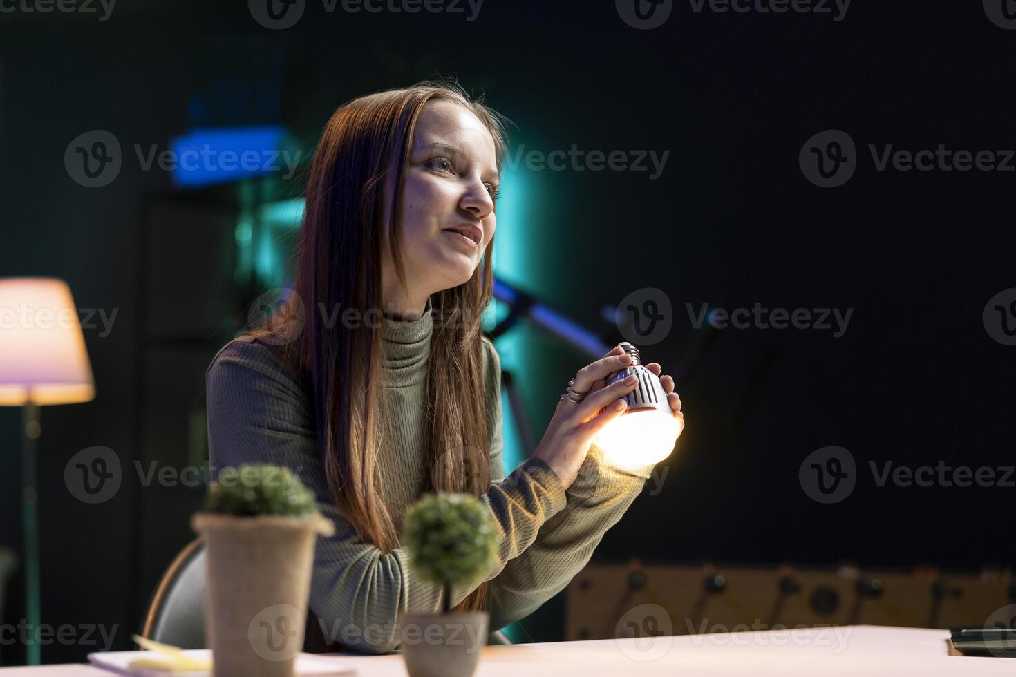 Young girl doing house improvement vlog, showcasing newly released smart light bulb to viewers. Gen Z content creator greeting viewers, presenting WIFI home automation photo