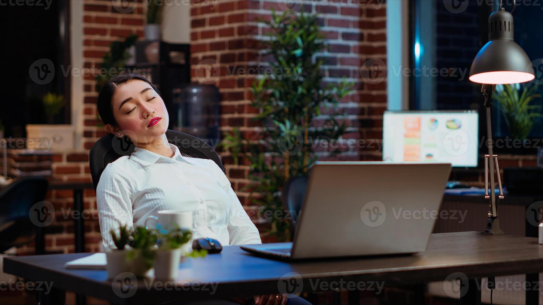 Tired employee asleep on computer desk chair suddenly waking up, struggling to finish writing emails. Drowsy businesswoman working overnight, typing on laptop, trying to stay awake, camera B photo