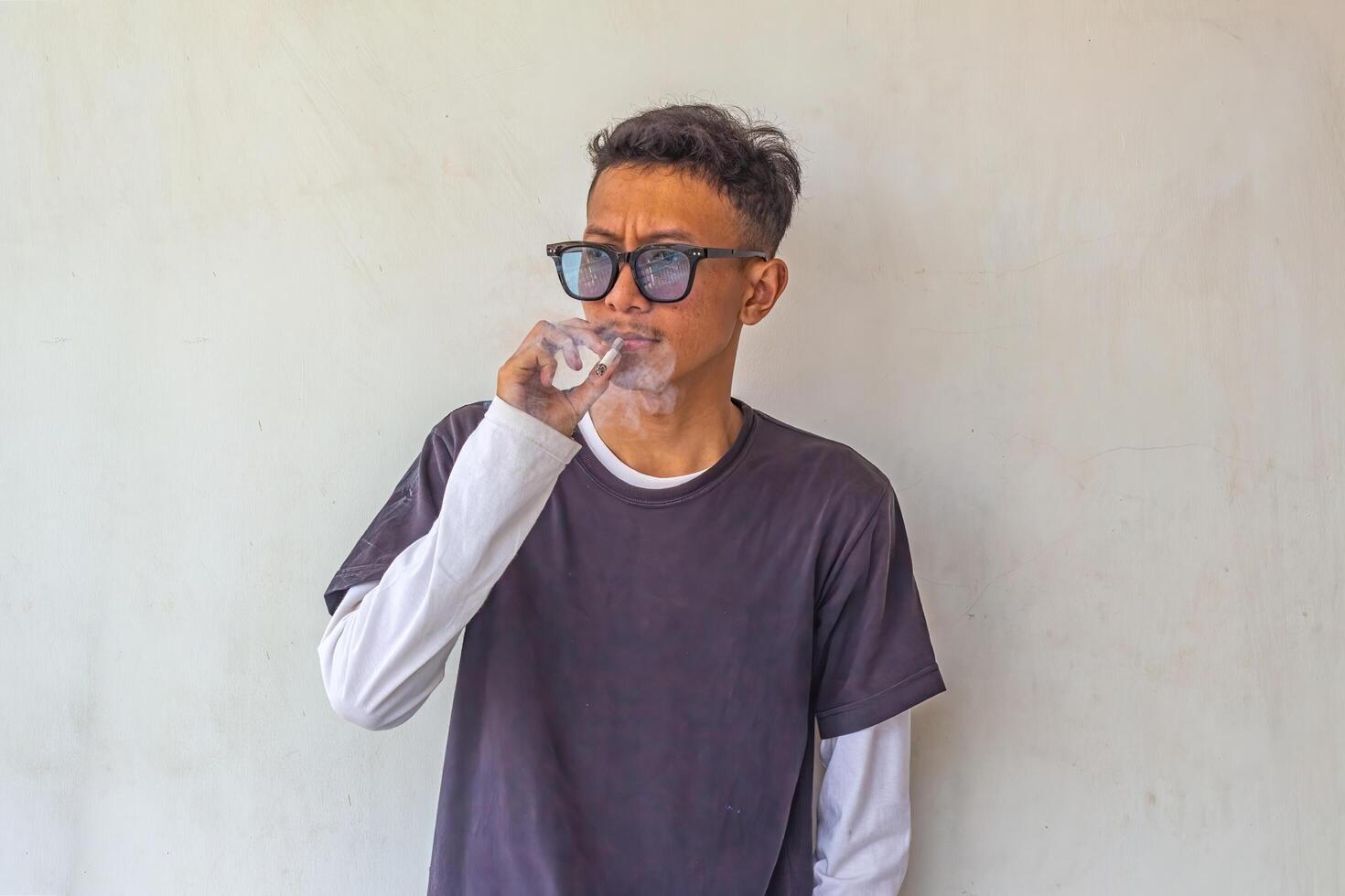a young man wearing a gray t-shirt with glasses is smoking isolated on white background. suitable for health and environmental concepts photo
