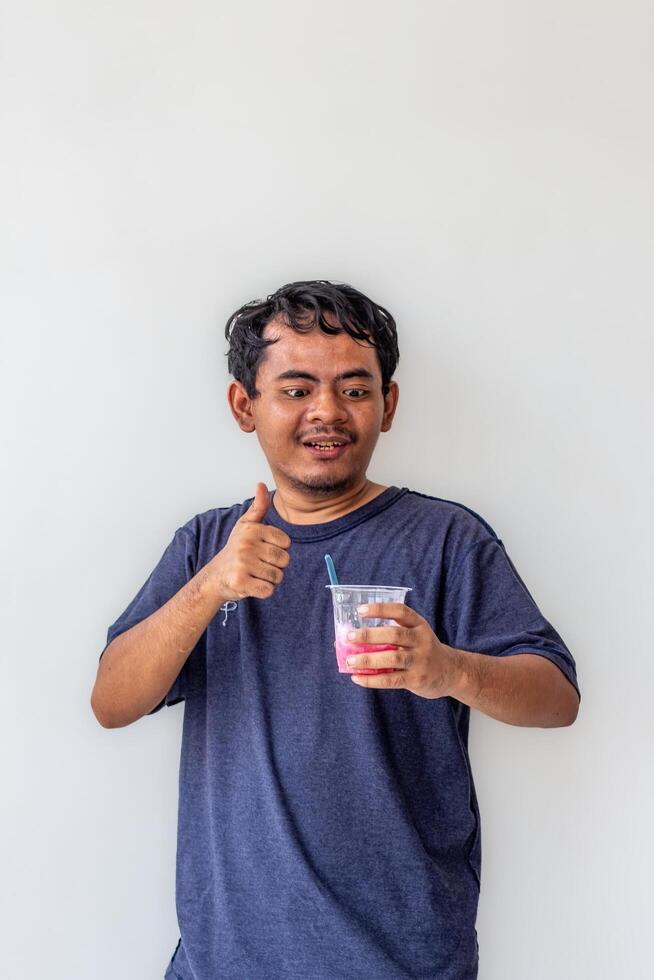 A young adult wearing a gray t-shirt and glasses is enjoying an Indonesian mixed iced drink or holding a plastic cup isolated on white background. for food content and health, and diabetes concepts photo