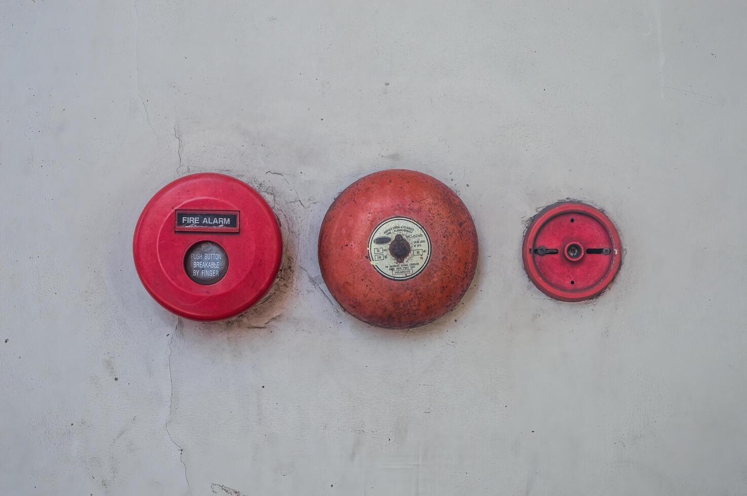 Retro fire alarm components attached to a white wall, such as a red break glass button and a bell. photo